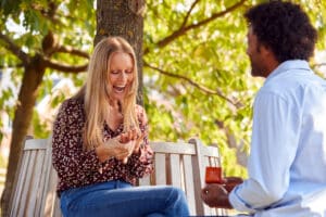 man proposing to woman outside on bench with beautiful engagement ring