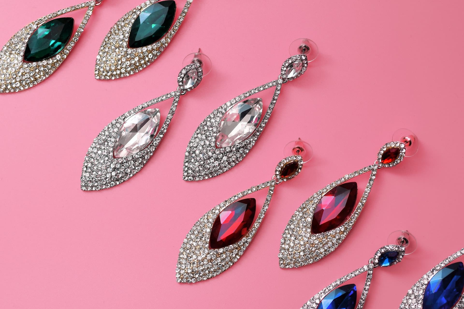 Many earrings with different gemstones against a pink background.